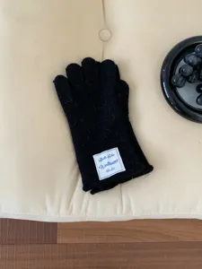 Vista dettagliata di guanti invernali in maglia nera con etichetta su sfondo beige imbottito.