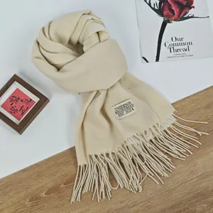 Detailansicht des warmen, beigefarbenen Kaschmirimitat-Schals mit Fransen und stilvollem Label.