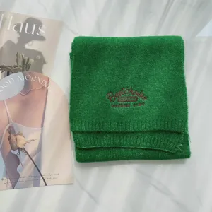 Grüner Strickschal Detail mit feiner brauner Stickerei und weicher Materialstruktur.