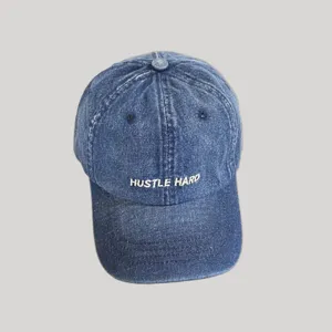 Nahaufnahme Detail der blauen Jeans Baseballkappe mit weißer HUSTLE HARD Stickerei vorne.
