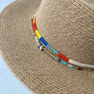 Sommerlicher Boho-Strohhut Detail mit bunten gewebten Fäden, Muscheln und Metallic-Verzierung.