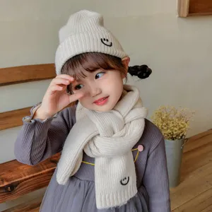 Cute kids knitted beanie hat and scarf set with sweet smile embroidery detail closeup.