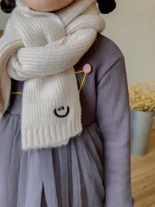 Children winter knitted scarf detail closeup showing soft warm fabric and cute smile embroidery.