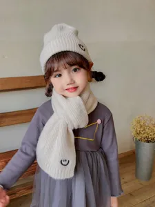 Cozy kids knit hat and scarf set in beige with cute embroidered smiley face detail.