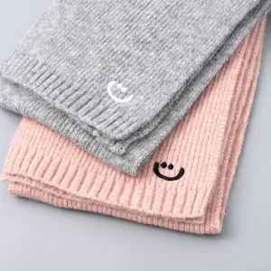 Close-up detail of children's knit scarf with cute embroidered smiley face, soft texture.