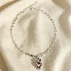Gros plan d'un délicat collier avec pendentif hibou argenté et cristaux étincelants.