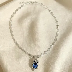 Collier ton argent avec chaîne florale délicate et pendentif hibou en cristal bleu.