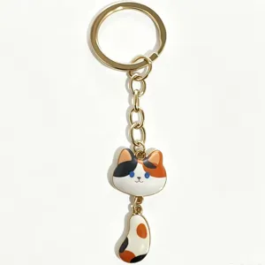 Cute calico cat keychain with dangling tail design, gold plated metal finish and enamel details.