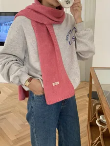 Nahaufnahme des rosa Strickschals mit einem gewebten Etikett fuer kuschelige Winterwaerme.