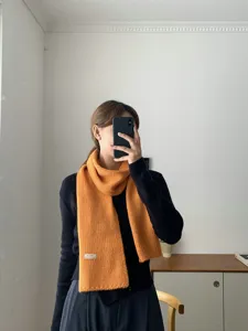 Nahaufnahme eines weichen orangefarbenen Strickschals im Winter, zeigt kuschelige Textur.