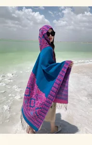 Vue de détail de la cape en tricot à capuche avec motif floral bleu et rose et franges.