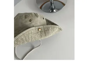 Detailed view of khaki outdoor sun hat with eyelets, snap brim and drawstring on white.