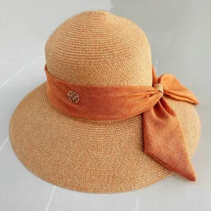 Gros plan detail du chapeau de paille d'ete pour femme avec ruban noeud orange et metallique.