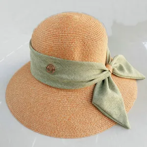 Vue détaillée d'un chapeau de paille d'été avec un ruban vert et un logo métallique.