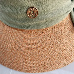 Détail de chapeau de paille d'été avec bord tissé, bandeau en tissu vert et logo M métallique.