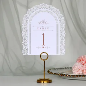 Elegante cartello numerato per tavolo da matrimonio ad arco bianco con supporto d'oro.