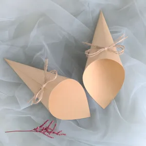 Detail shot of kraft paper confetti cones with rustic twine bow on soft white tulle fabric.