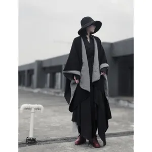 Vista di dettaglio di un poncho reversibile nero e grigio all'aperto, design con spacchi.