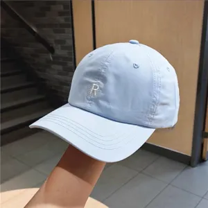 Light blue baseball cap detail, featuring a delicate embroidered letter R on front.