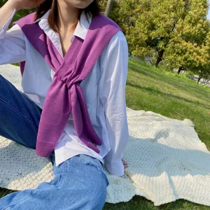 Detail shot of the stylish purple knitted shawl worn outdoors on grass in daily life.