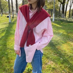 Detail view of the stylish red knitted shawl scarf worn over a pink shirt outdoors.