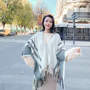 Detailed view of women hooded knitted poncho with striped pattern and fringe hem.