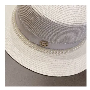 Close-up detail of white straw hat featuring elegant pearl trim and sparkling ribbon accent.