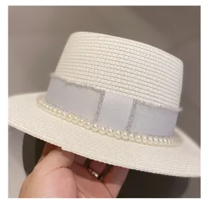 Detail view of a white straw boater hat featuring elegant pearl trim and a silver ribbon accent.