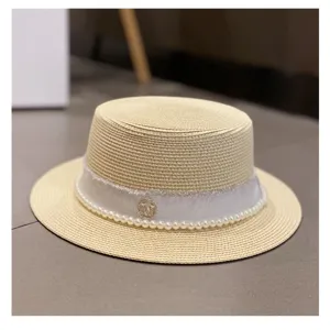 Closeup of summer women straw hat detail, featuring elegant white pearl ribbon and chic metal logo.