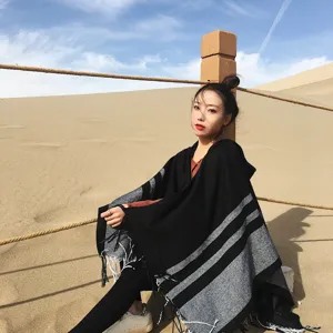 Outdoor detail view of a black and grey striped hooded cape with chic tassels for winter wear.