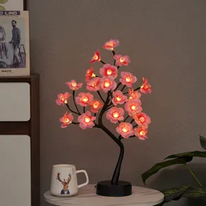 Detailopname van LED bloemboamlamp met roze bloesems en warm licht op kleine tafel.