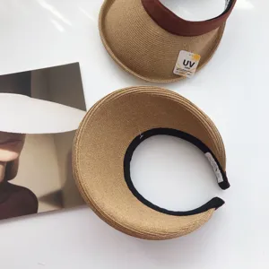 Vista detallada de la visera solar de paja con diseño abierto, banda marrón y etiqueta UV.