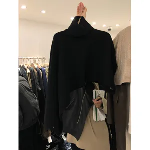 Vista dettagliata del poncho in maglia nera a collo alto con orlo asimmetrico da donna.