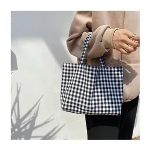 Detail view of a small black and white checkered gingham tote bag held by a model