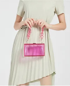 Detailed view of a pink transparent acrylic clutch bag held by a model in a dress