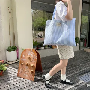 Φωτογραφία lifestyle σε εξωτερικό χώρο με μπλε ριγέ πάνινη τσάντα που κρατά μια γυναίκα.