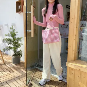 Detail view of a pink and white gingham cotton tote bag held by a model in a cafe setting
