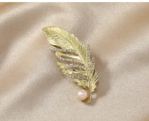 Exquisite gold feather brooch detail with sparkling rhinestones and a single pearl accent.