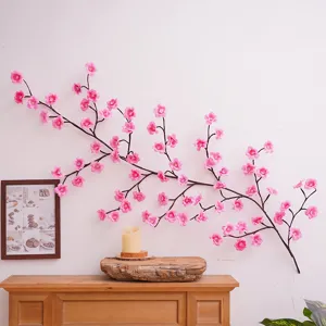 Nahaufnahme der künstlichen rosa Pflaumenblüten LED Zweiglampe an einer weißen Wand.