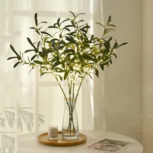 Artificial olive branches with fairy lights in glass vase for home wedding room decor.