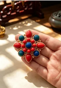 Primo piano di una spilla etnica a forma di loto con pietre colorate e finitura oro.