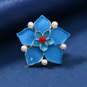 Detailed view of vintage blue enamel flower brooch featuring pearl accents and red stone center.
