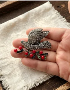 Close-up detail shot of a vintage crystal rhinestone dove brooch with red berries in hand.