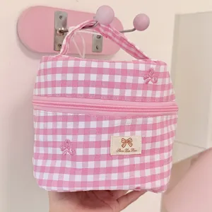 Close-up of pink gingham cosmetic bag with embroidered bows, hanging on a wall hook, detail view.