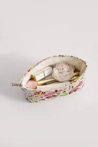Detailed view of floral fabric makeup pouch with interior cosmetic props and smooth metal zipper.