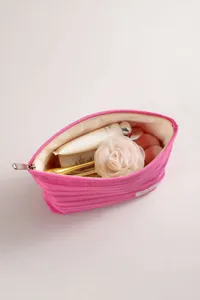 Vista detallada del bolso de maquillaje a rayas rosas relleno con tubos de crema y una rosa.