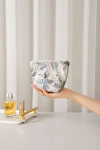 Detail view of a blue floral jacquard cosmetic bag with golden threads and a zipper closure.