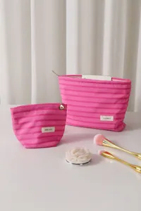 Vista detallada del juego de bolsas cosméticas de rayas rosas con pinceles en mesa.