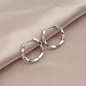 Detail shot of silver mobius twisted hoop earrings on satin fabric, elegant design.