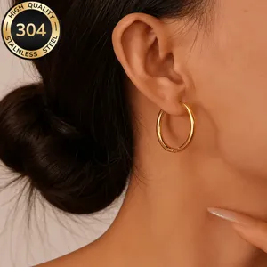 Detail shot of stainless steel gold-plated hoop earrings worn on ear, smooth and elegant.